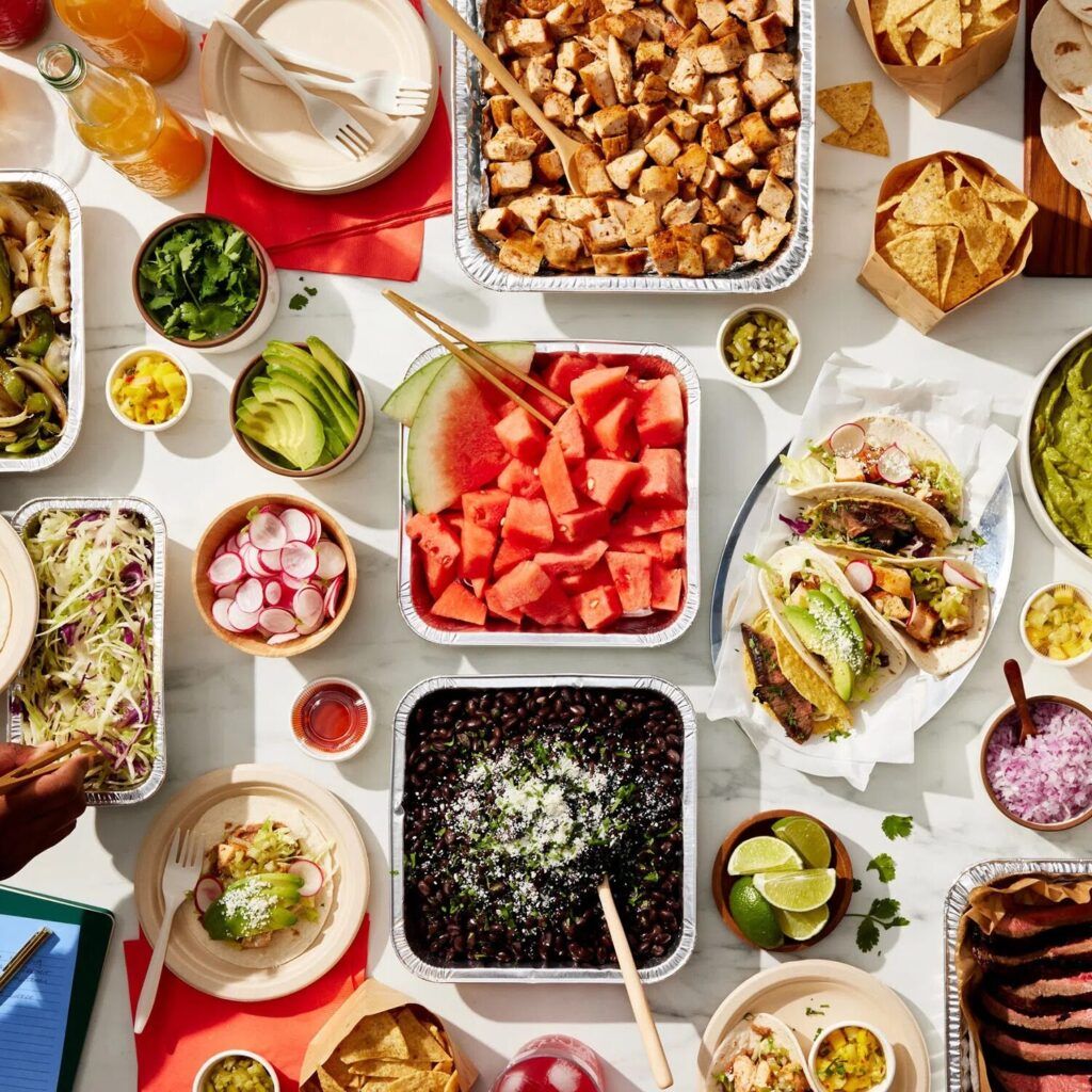 Catering platters of watermelon, tacos, black beans, limes, and different Mexican dishes